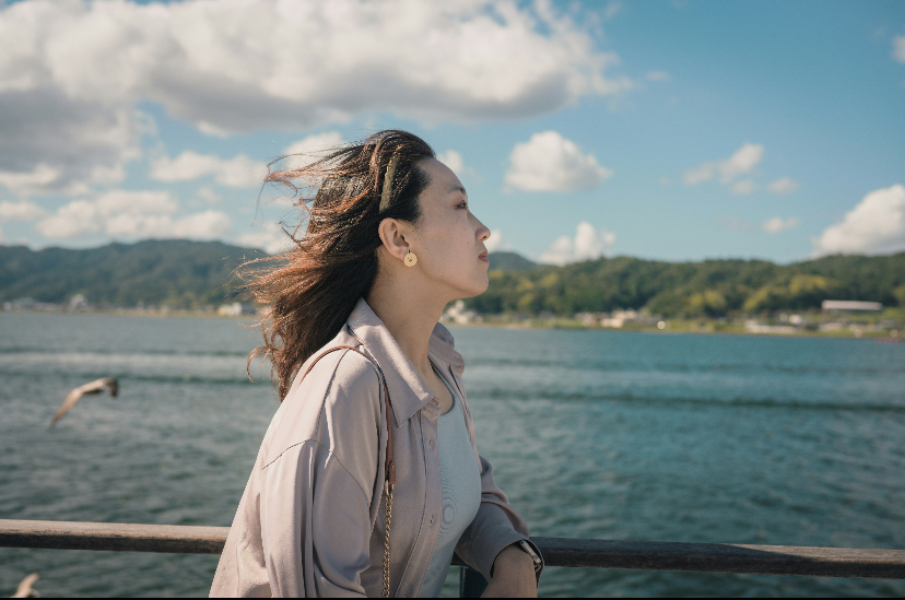 Woman standing by the sea with the wind in her hair, looking out at the water